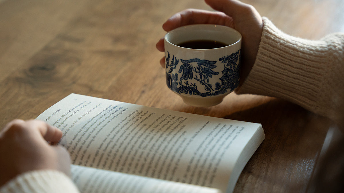 Person holding a cup of coffee while reading a book